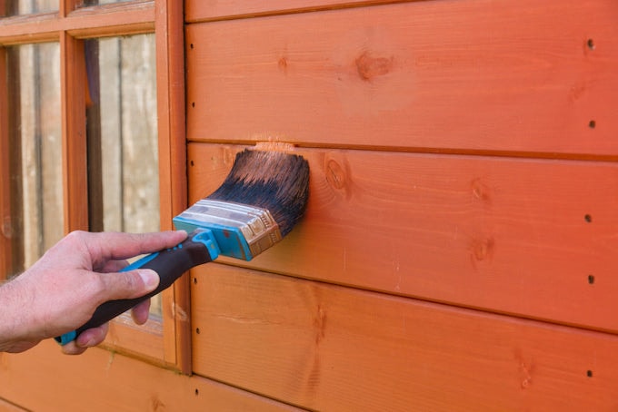 Applying wood treatment to shed exterior
