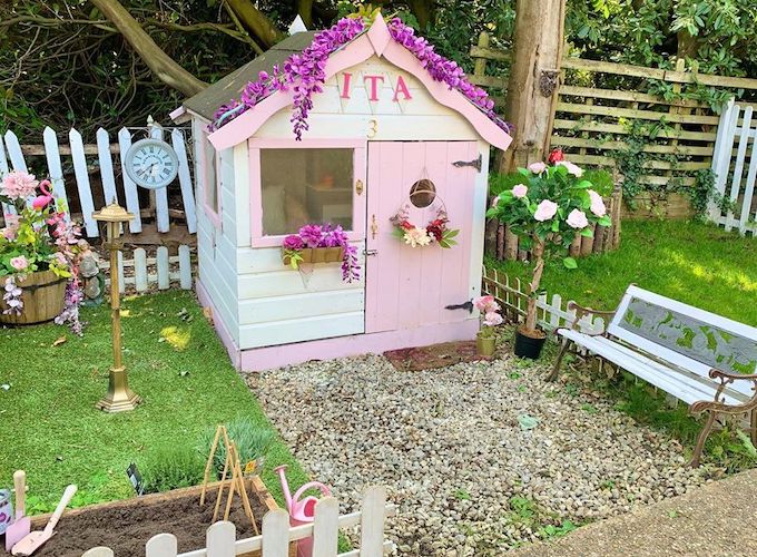 Pink and white painted playhouse with floral decorations and bench