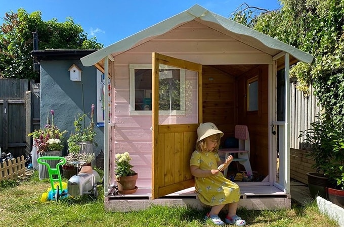 Pink and white playhouse with little girl sitting on stoop