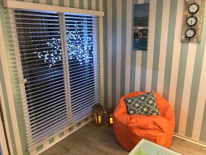 Orange bean bag with striped wallpaper and large window inside summer house