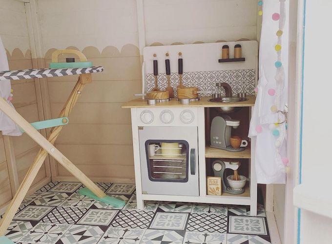 Toy kitchen inside Waltons playhouse with decorated flooring and ironing board
