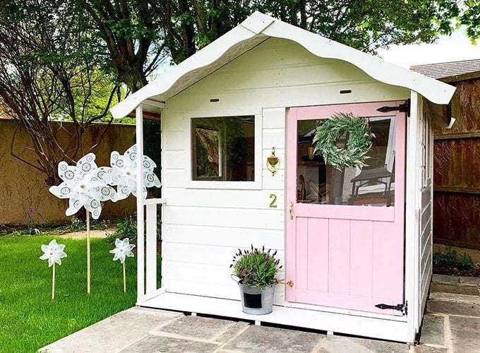 Pink and cream playhouse with white pinwheels and lavender potted plants