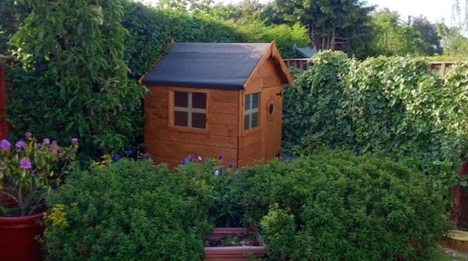 Unpainted Waltons playhouse surrounded by greenery