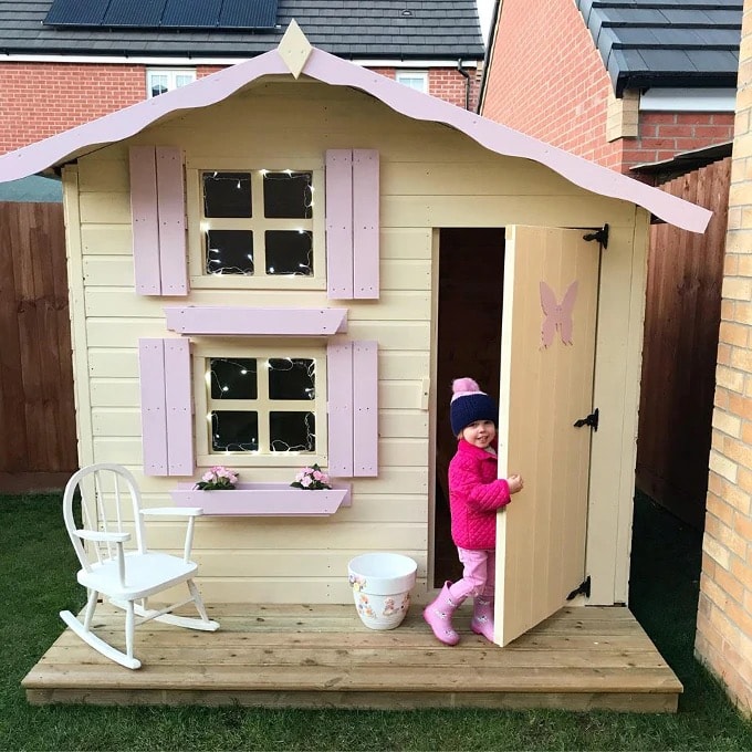 Little girl standing in front of a cream and pink Snowdrop playhouse
