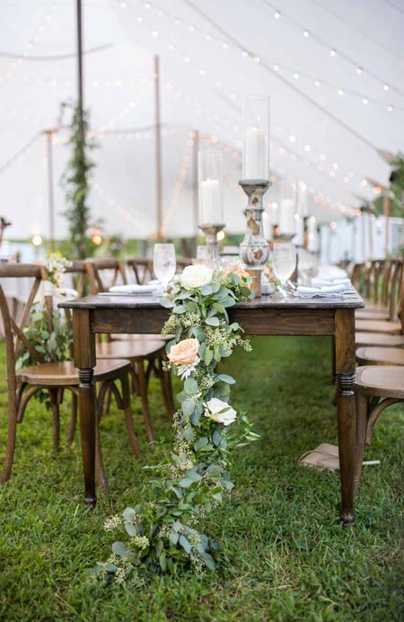 Delicate backyard wedding tablescape with candles, greenery and white blooms, white linens and string lights