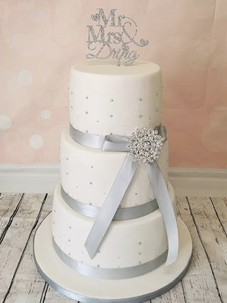 silver glittery mr and mrs wedding topper and wedding cake decorated with ribbon bow and embellishment
