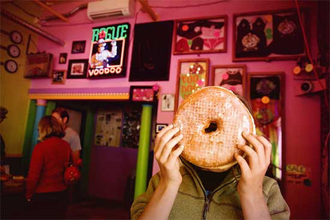 A man holding a giant doughnut over his face at Voodoo Doughnuts in Portland