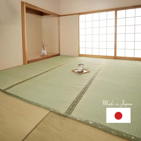 A traditional Japanese room with tatami flooring. The room features shoji sliding doors made of translucent paper framed with wood, allowing soft light to enter. In the corner is a small alcove (tokonoma) with a simple vase holding a few delicate branches. Centrally placed on the tatami floor is a wooden tray with a ceramic teacup, suggesting a setting for a quiet tea moment. The overall ambiance is serene and minimalistic, characteristic of Japanese interior design.