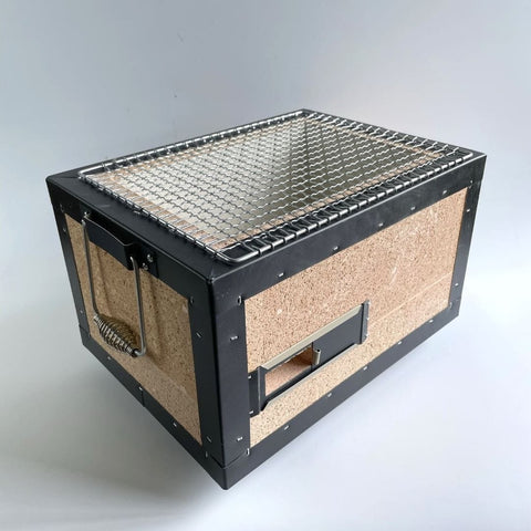 A compact, portable charcoal grill with a metal grate and cork insulation on the sides, set against a plain background.