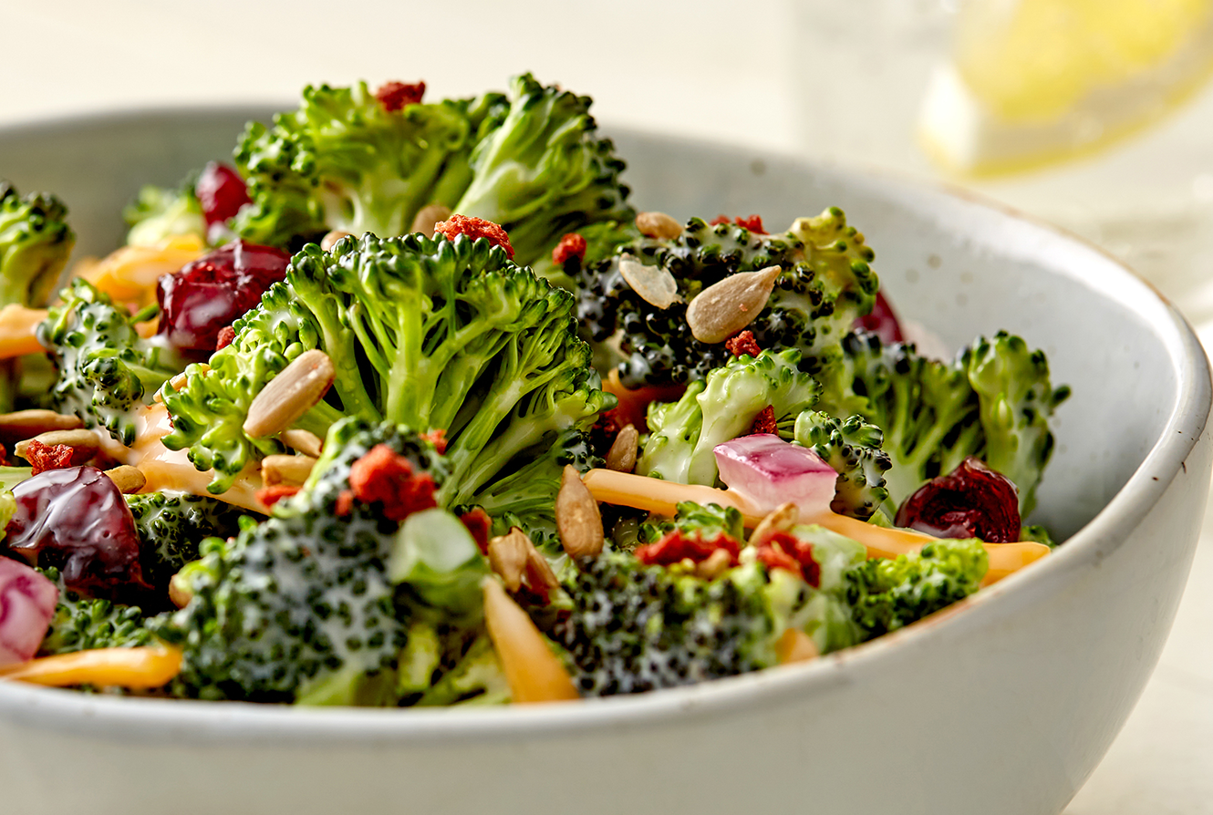 A bowl of broccoli salad with red onions and cheddar.
