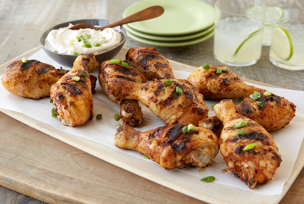 A platter of grilled chicken thighs, a dish of dipping sauce, plates, and filled drinking glasses.