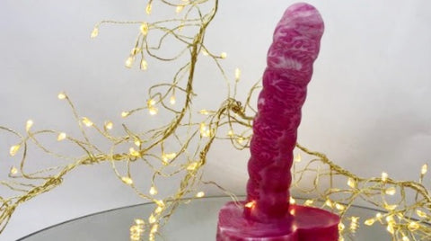 A pink and white anal dildo with fairy lights in the background