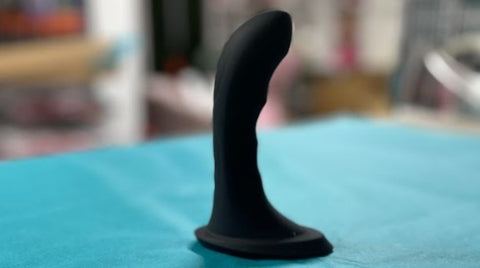 a black prostate massager with a curved tip on turquise tissue paper. 