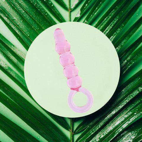 Pink glass dildo with ripples on green plant background