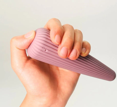 A hand holding a pale pink vibrator with a ribbed, tapered shaft