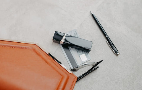 A lipstick vibrator in a black case, a black pen, a crediD card and a purse in light tan leather