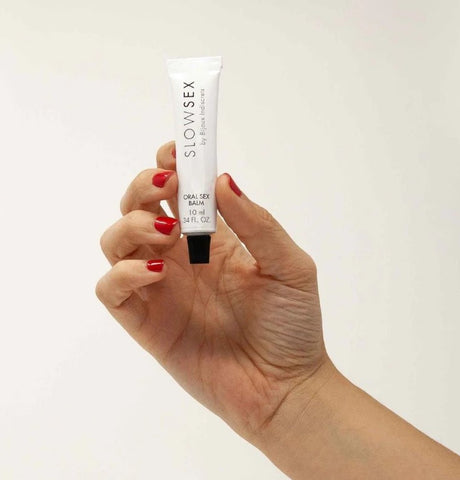 A hand holding a tube of Slow Sex Oral Sex Balm