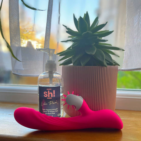 Nymph clit-licking rabbit next to a bottle of Sh! Pure lube and a succulent in a pink plant pot