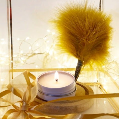 An atmospheric photo in gold hues, with a lit candle and a soft feather pom