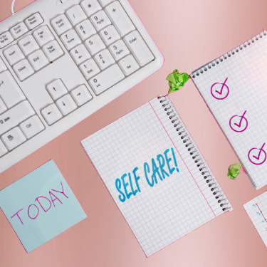 a desk with note pads and a keyboard and a note that says Self Care!