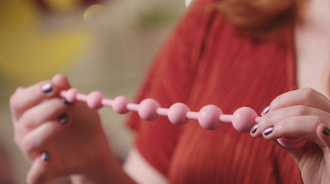 a pair of hands holding a pink string of anal beads