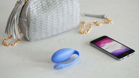 A powder blue We-Vibe Jive vibrator surrounded by a smartphone and a grey handbag.