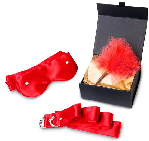 A black gift box with gold tissue paper. Red satin ties, a red blindfold and a red feather pom.