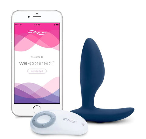 We-Vibe Ditto butt plug is smooth dark blue silicone, next to a smart phone and white plastic remote contro