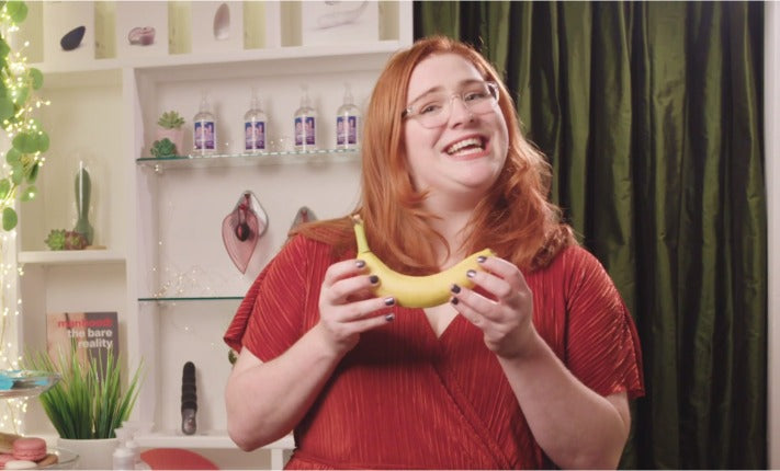 Sex Educator Evie in the sex shop, holding a banana and looking very happy
