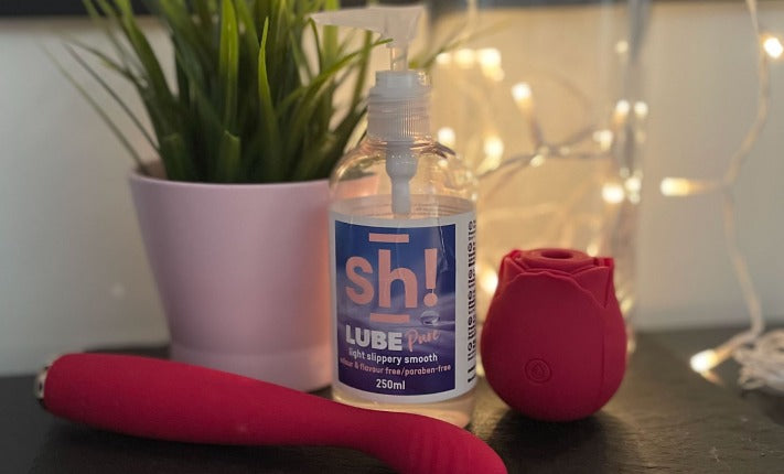 A green plant in a pink pot, a red g-spot vibratot, a bottle of Sh! lube and and a rose suction toy. Fairylights in te background.