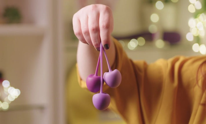 A hand holding three love balls in shades of purple