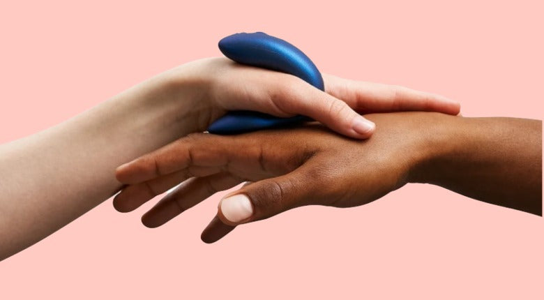 blush pink background. One white hand plus one brown hand tpocuhing each other and holding a blue C-shaped vibrator