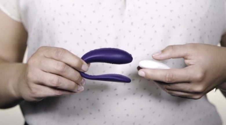 A person in a light top holds a purple Unite couples vibrator + remote control