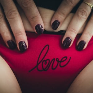a pair of hands resting on red knickers with the word love on the front