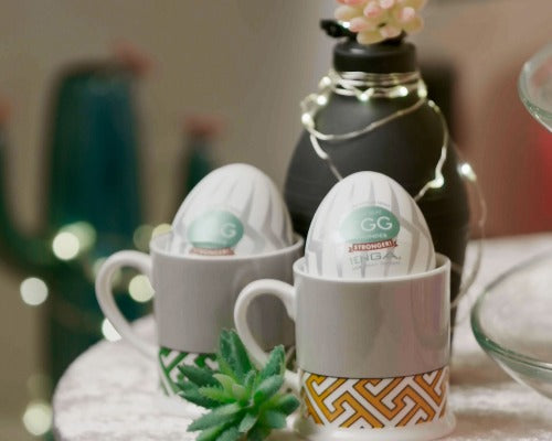 a table with a douche and two tenga eggs in tiny china espresso cups