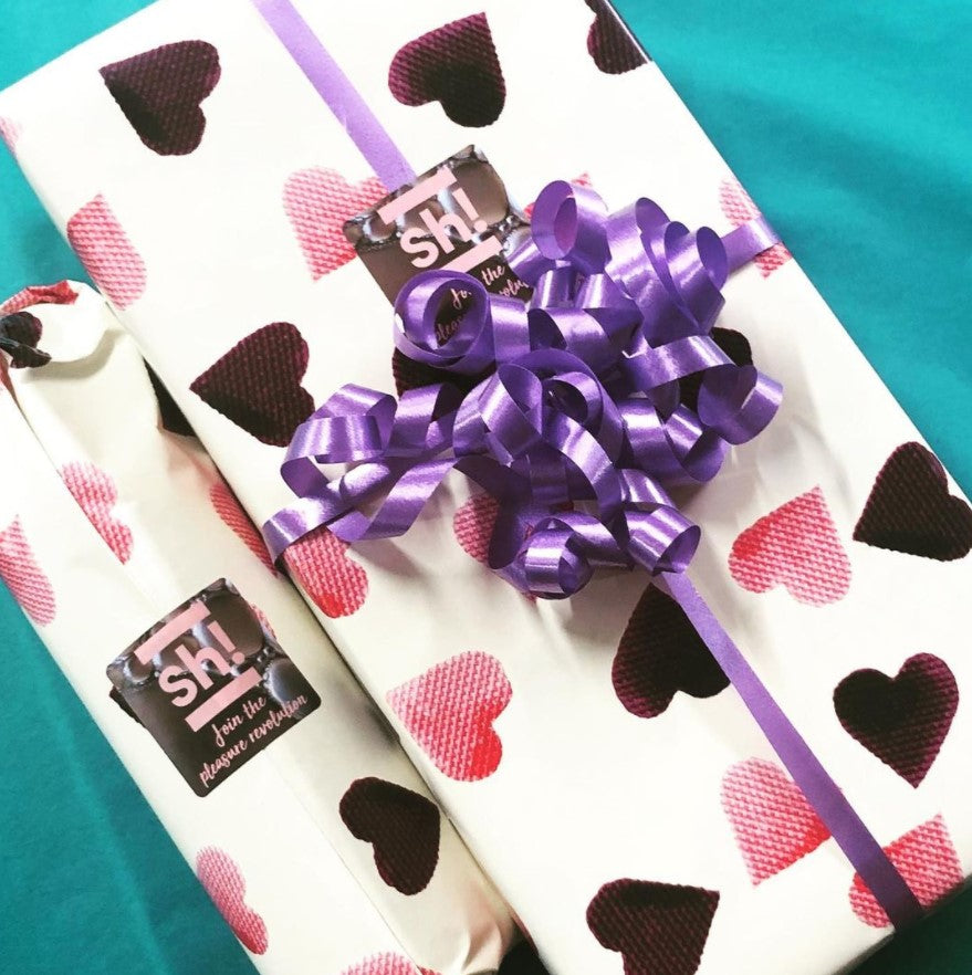 Two gifts wrapped up in paper with pink and purple hearts. 