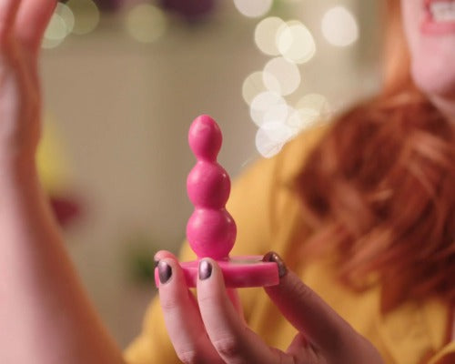 a hand holding a bright pink buttplug with 3 bubbles of increasing sizes