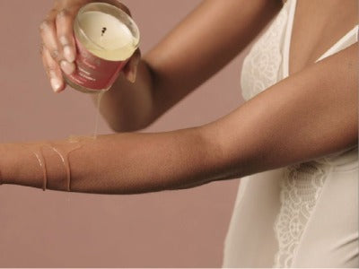A brown hand poring melted massage wax / oil over brown arm
