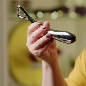 A hand holding a stainless steel dildo - Sh! Women's Store 