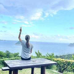A woman on top of a mountain, looking at the Hong Kong seas views on a picnic table, giving the peace sign. 