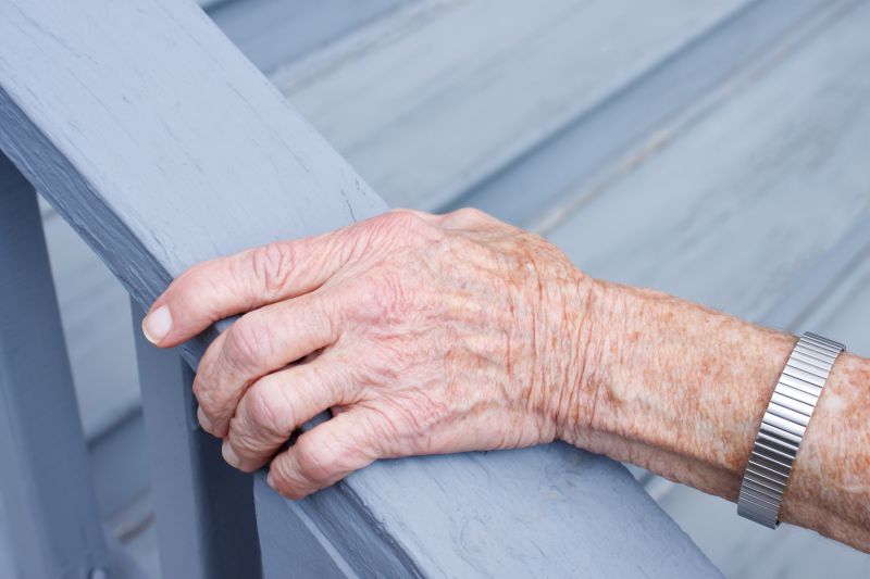 An elderly hand on the railing of a deck.