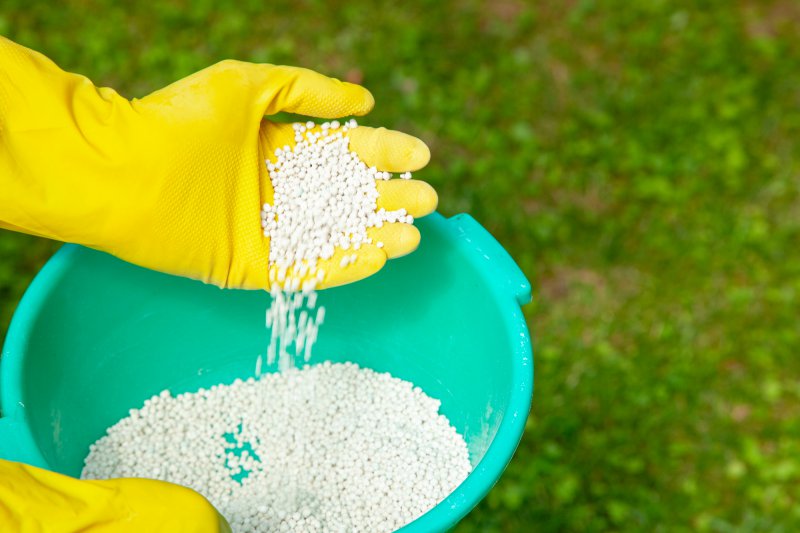 A hand dumping yard fertilizer into a bucket.