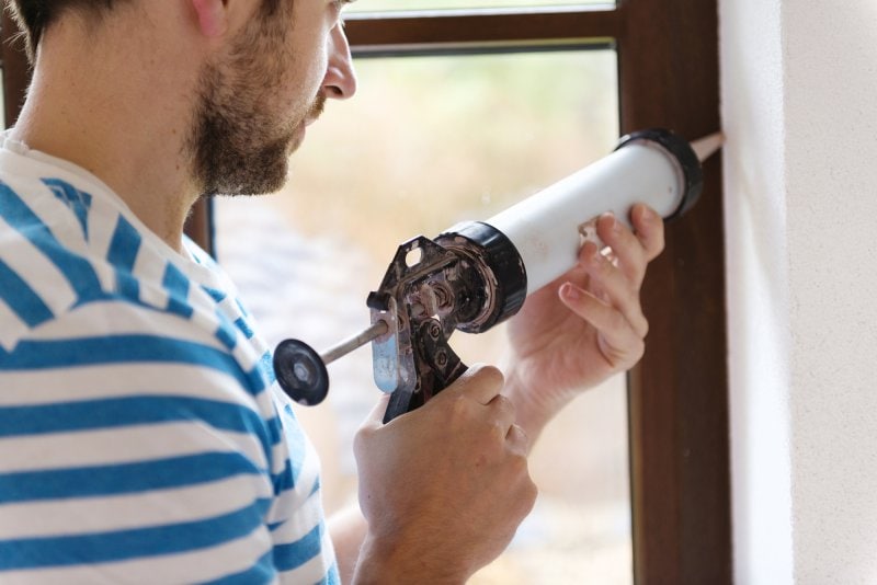 A man caulking his window to prevent air leaks.