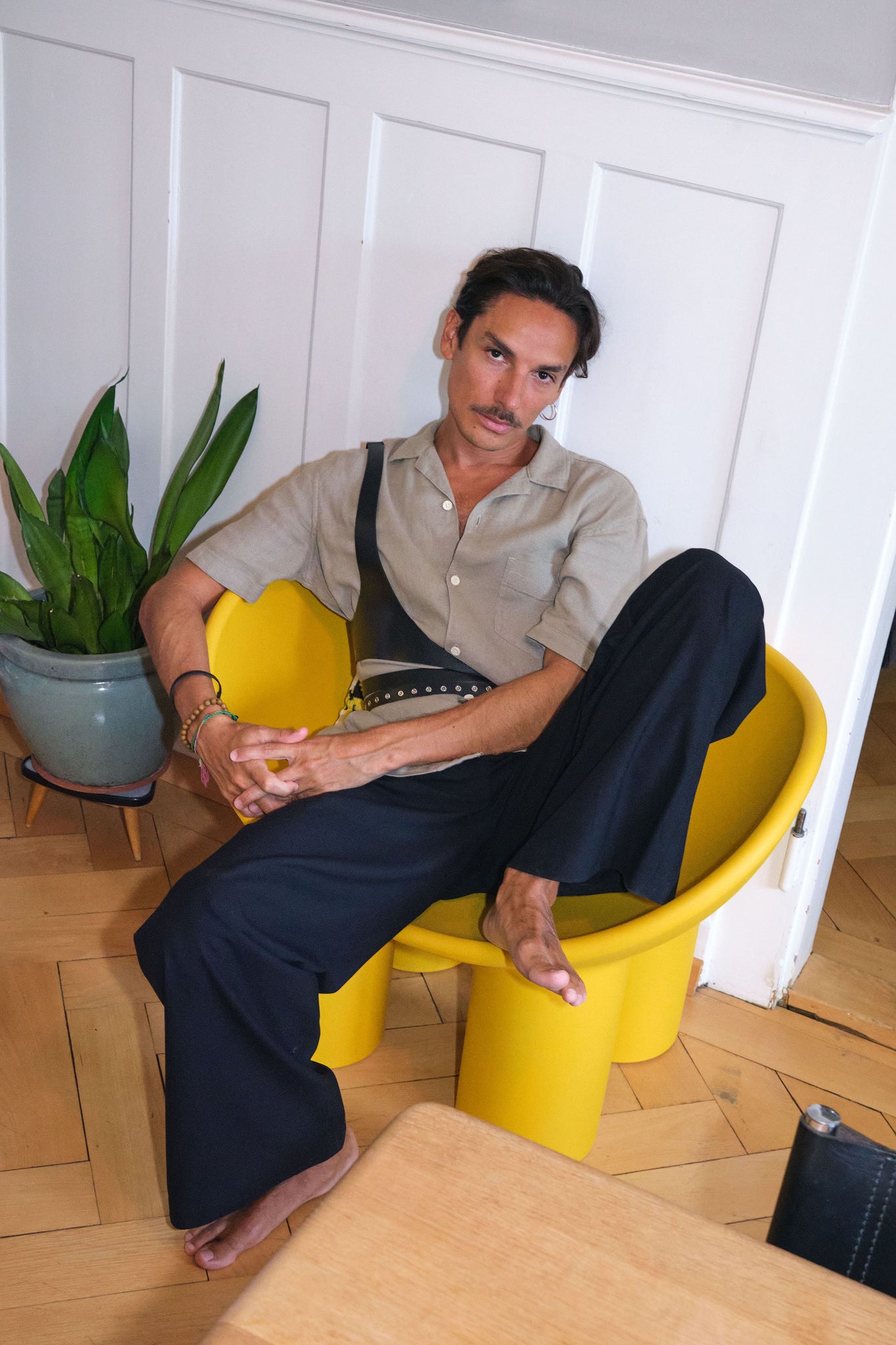 man sitting on yellow armchair wearing yvy leather asymmetric bodypiece