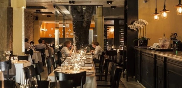 Uma grande mesa no interior do restaurante iluminado com duas pessoas a fundo jantando.