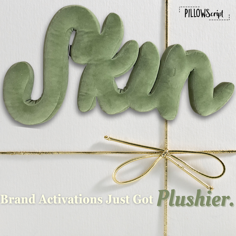 Gift box that has a custom plush green script pillow in the word shape of skin that says Brand Activations just got plushier.