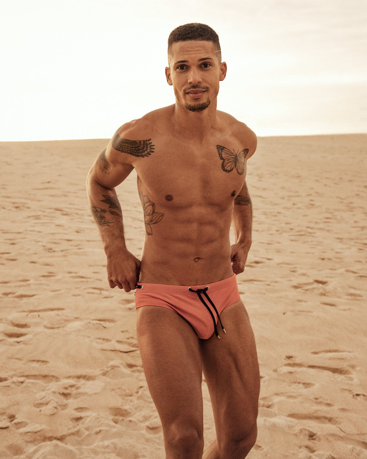 young black man with tattoos wearing mens swim briefs on beach