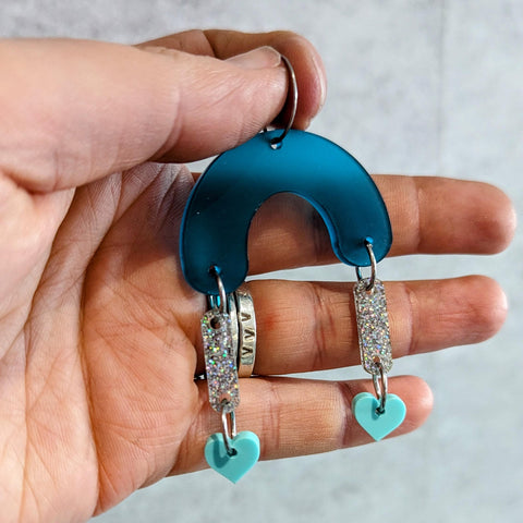 An earring made from a blue acrylic arch, glitter bars and mint green hearts on the end. Created on a corporate wellbeing day ran by Lady And The Laser Beam