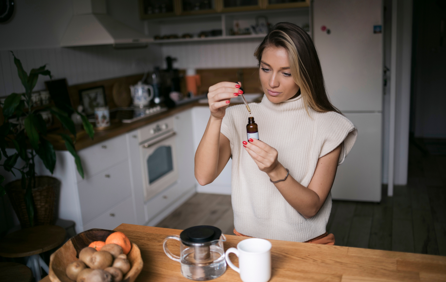 Woman holding tincture bottle of CBD in front of a table with tea