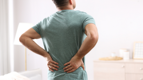 A man in a green t-shirt holds his back in pain